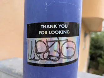 A rectangular sticker affixed to a dark purple pole. The sticker features a black background on its upper and lower sections. The top black section displays the white, sans-serif text 'THANK YOU FOR LOOKING'. The central part of the sticker is a prominent holographic panel, which reflects light in iridescent colors. Overlaid on this holographic surface is a complex, abstract design composed of thick, looping black lines, which appear to form a highly stylized word or symbol, possibly 'LOOKING' or 'LOGO'. The overall appearance suggests a blend of text and abstract art.
