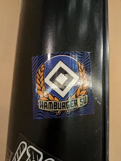 A sticker featuring the logo of Hamburger SV, a German football club. The logo is a diamond shape with a smaller diamond inside, surrounded by wheat stalks.  The text "Hamburger SV" is written below the logo.