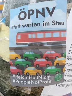A sticker advocating for public transportation. It depicts a train contrasted with cars stuck in traffic. Hashtags promote social movements.