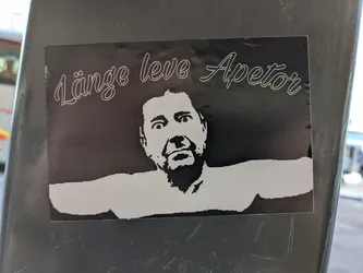 Black and white sticker featuring a stylized portrait of a man with the text "Länge leve Apetör" written above him. The man's arms are outstretched.