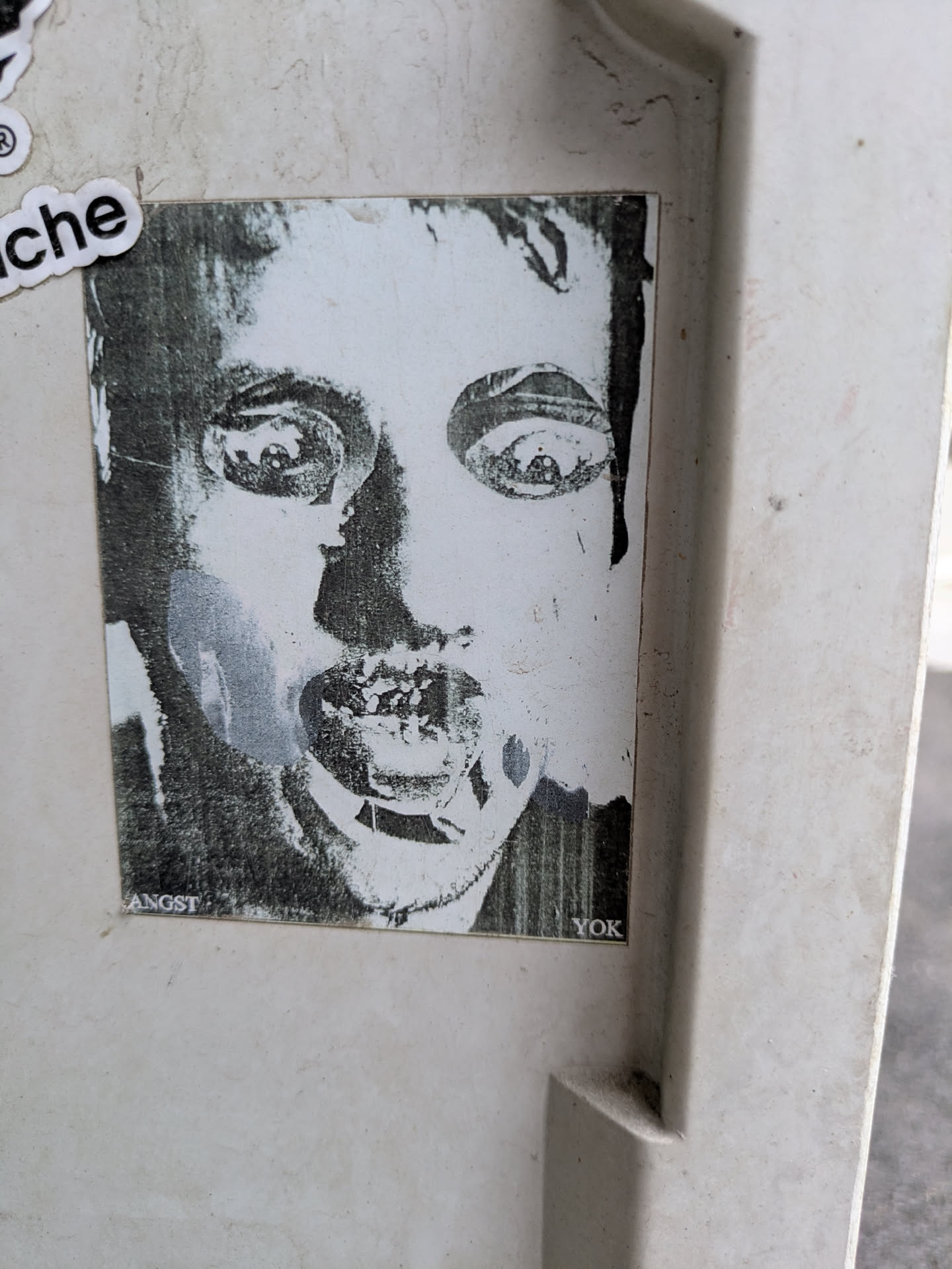 This is a monochrome sticker with a grainy, distressed appearance. It features a face with wide eyes and an open mouth, giving it a striking and unsettling look. The text "ANGST" and "YOK" are at the bottom.