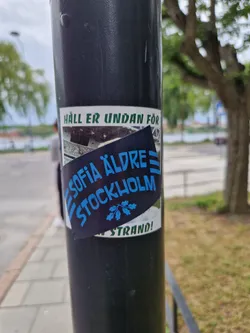 A sticker featuring the text "Sofia Äldre Stockholm" and an image of a bridge.  The top of the sticker also reads "Håll er undan för". The bottom part of the sticker says "Strand!"