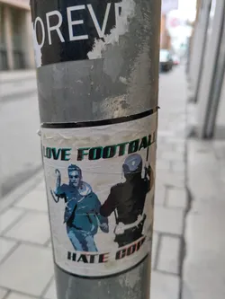 A sticker depicting a man running away from a police officer. The sticker's text is  "Love Football Hate Cops".