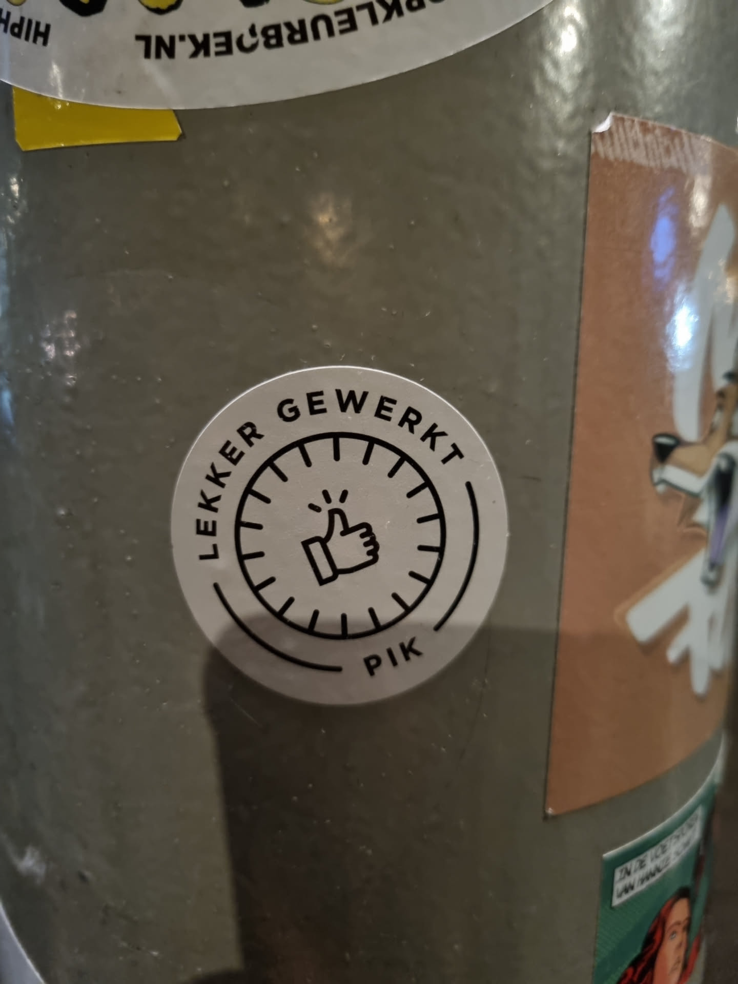 A round sticker with a thumbs up symbol inside a circular design. The text "Lekker Gewerkt" which translates from Dutch to "Well Done" is written around the circle. At the bottom, it says PIK. 