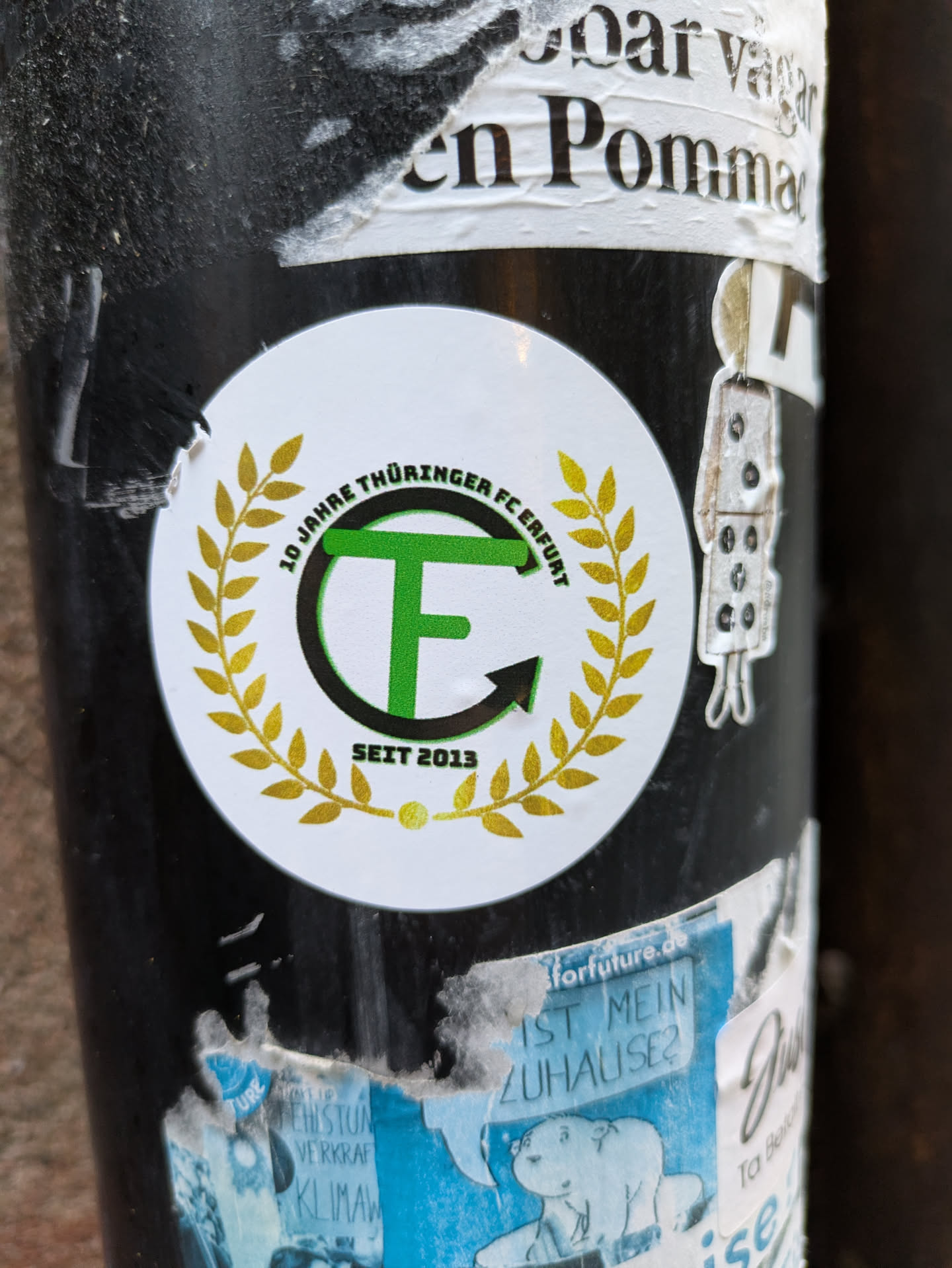 A round sticker commemorating 10 years of Thüringer FCE Erfurt (since 2013). It features a green and gold logo with the letters 'T' and 'F' inside a circular design encircled by a laurel wreath. 