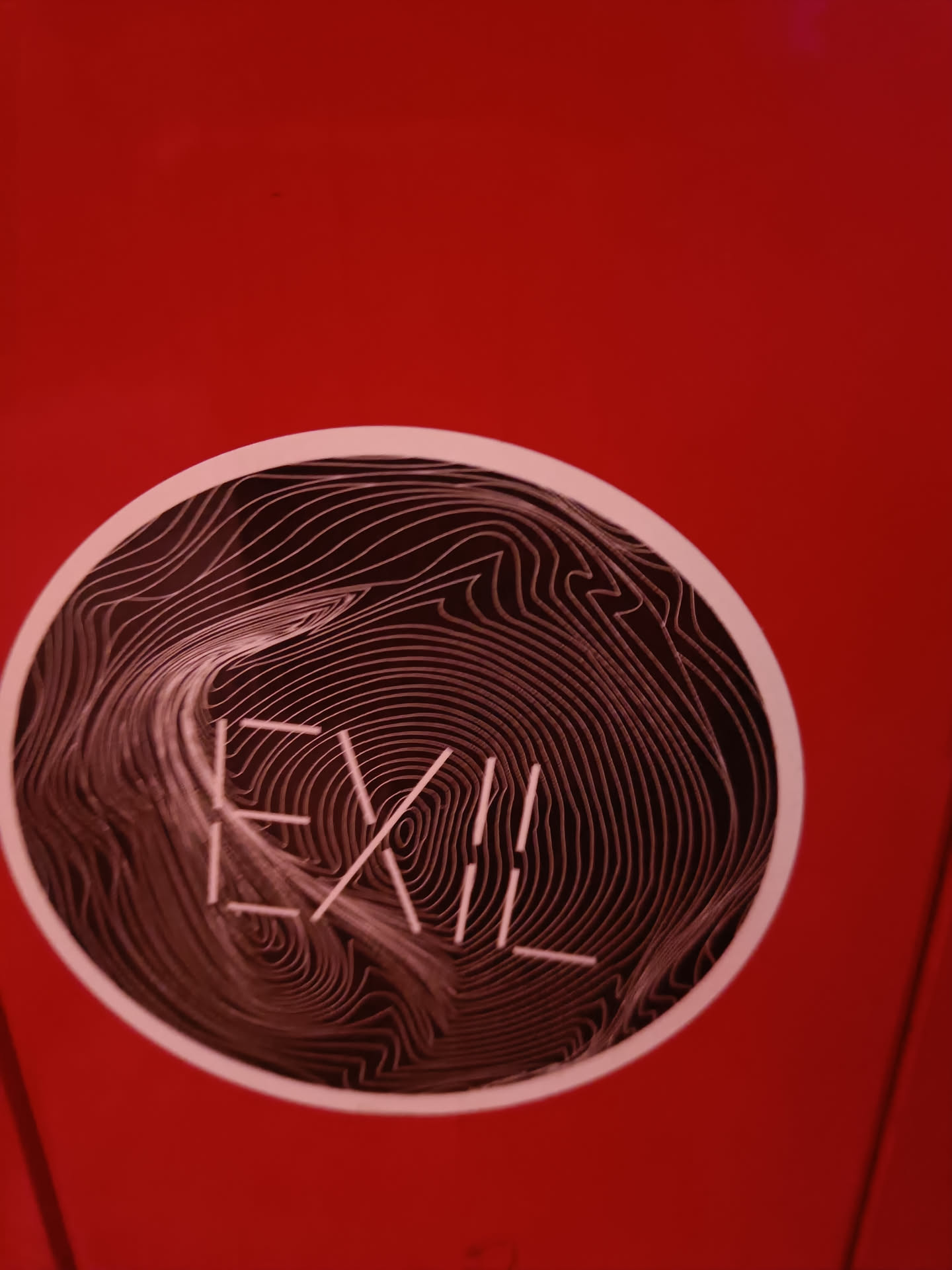 Round sticker with the word EXII in the center. The background is a topographic-like design in shades of dark red and white.  The word EXII is written with thin, light colored lines that appear raised from the surface.