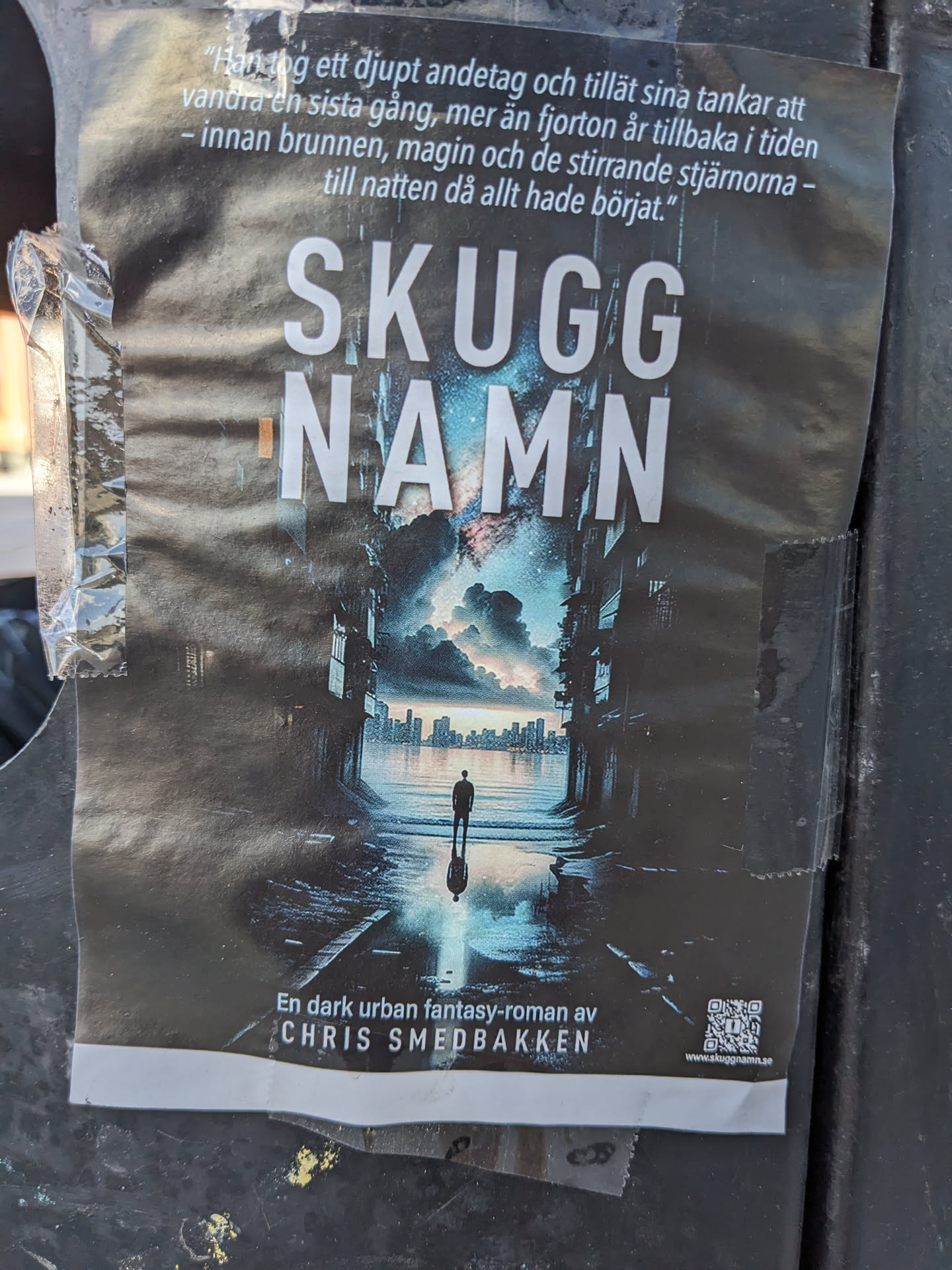 A book cover sticker for the novel "Skugg Namn" by Chris Smedbakken.  The image shows a person standing in a dark, urban setting with a city skyline visible in the distance. The text is in Swedish and it translates to "Shadow Name".