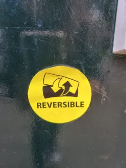 A round yellow sticker with black text and a simple graphic depicting something reversible. The text "REVERSIBLE" is clearly visible.