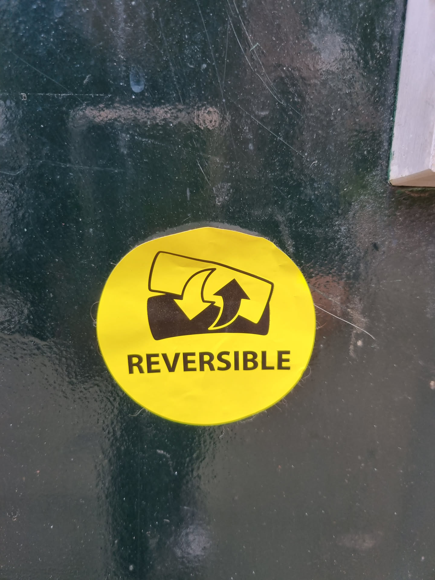 A round yellow sticker with black text and a simple graphic depicting something reversible. The text "REVERSIBLE" is clearly visible.