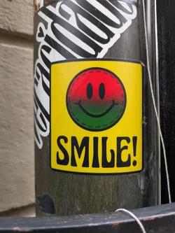 A yellow sticker with a tri-color smiley face and the word SMILE! in bold black letters. The smiley face is red, orange, and green.