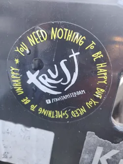 Round black and yellow sticker with the word "Trust" in the center and a phrase around it. It also contains a Facebook social media link.