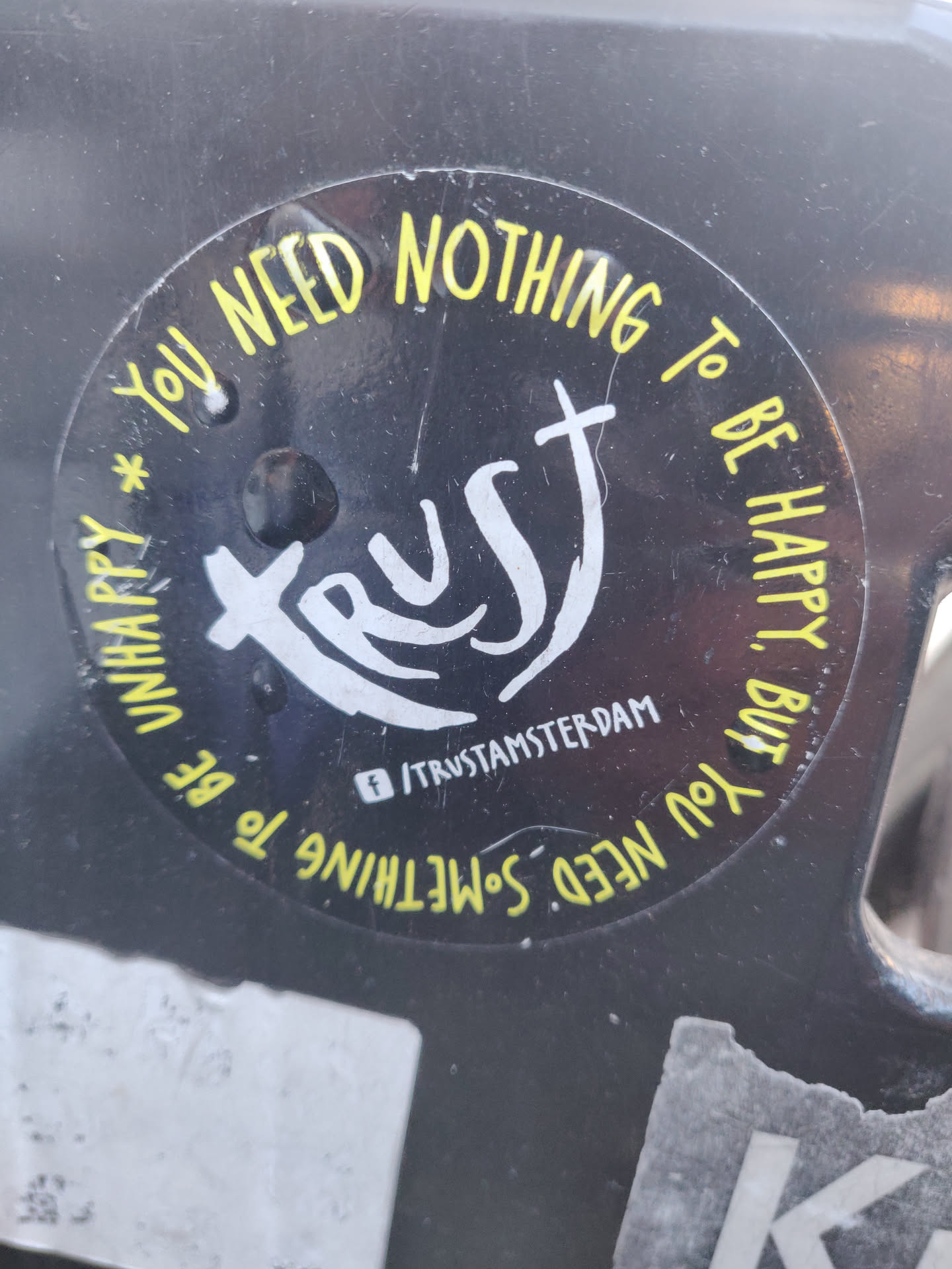 Round black and yellow sticker with the word "Trust" in the center and a phrase around it. It also contains a Facebook social media link.