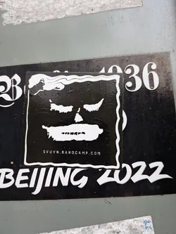 Street sticker A square, high-contrast black sticker featuring a stylized, shadowy face in white. The face has squinted eyes, a small nose cavity, and a smeared white mouth with jagged hints of teeth. A wavy white border frames the design, curving at the top left into fluid, cloud-like ripples. Below the face, the URL 'SVUVN.BANDCAMP.COM' is printed in small, clean uppercase lettering.