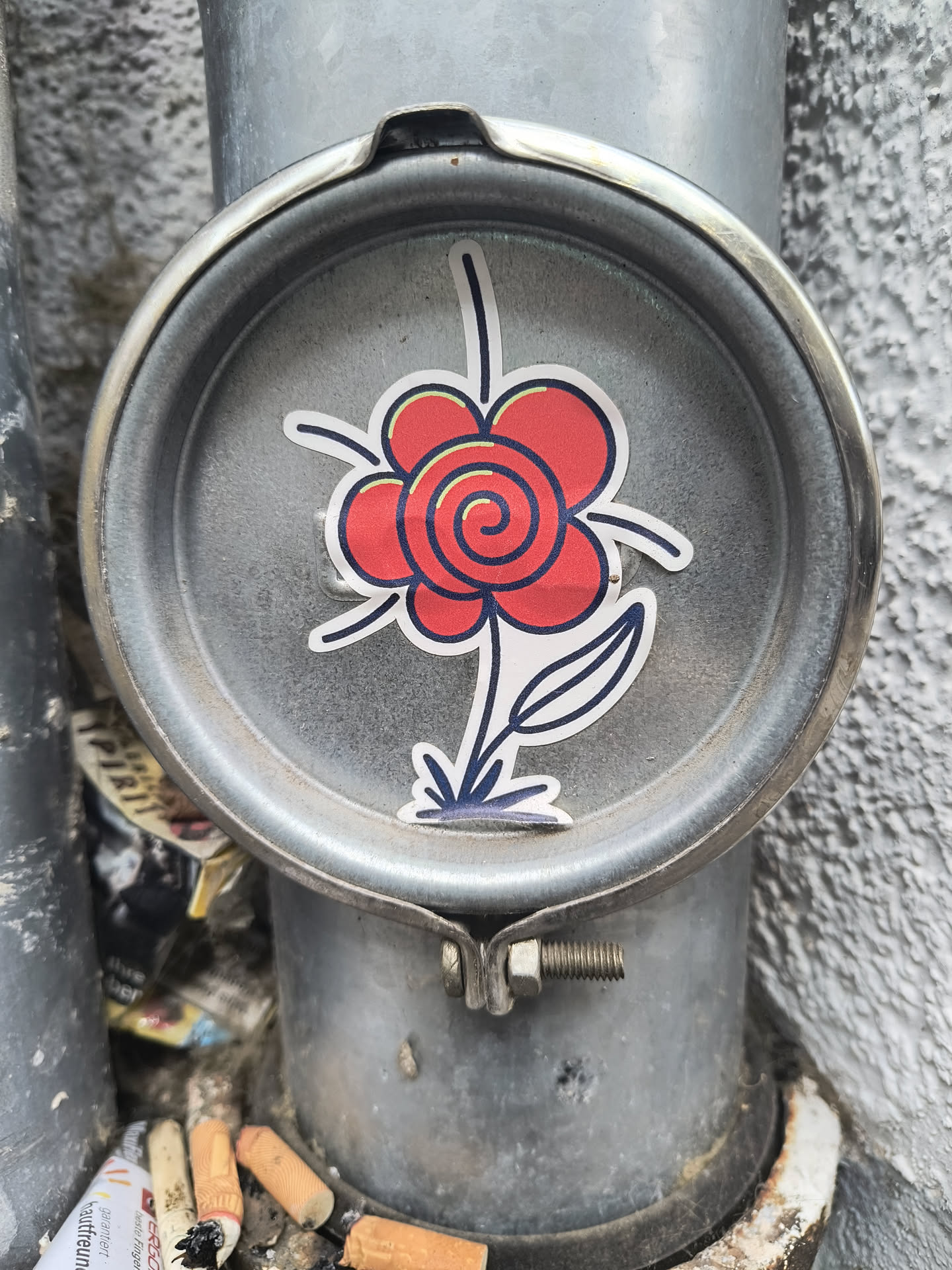 A red flower sticker with a spiral in the center is placed on a metal fixture attached to a pipe.