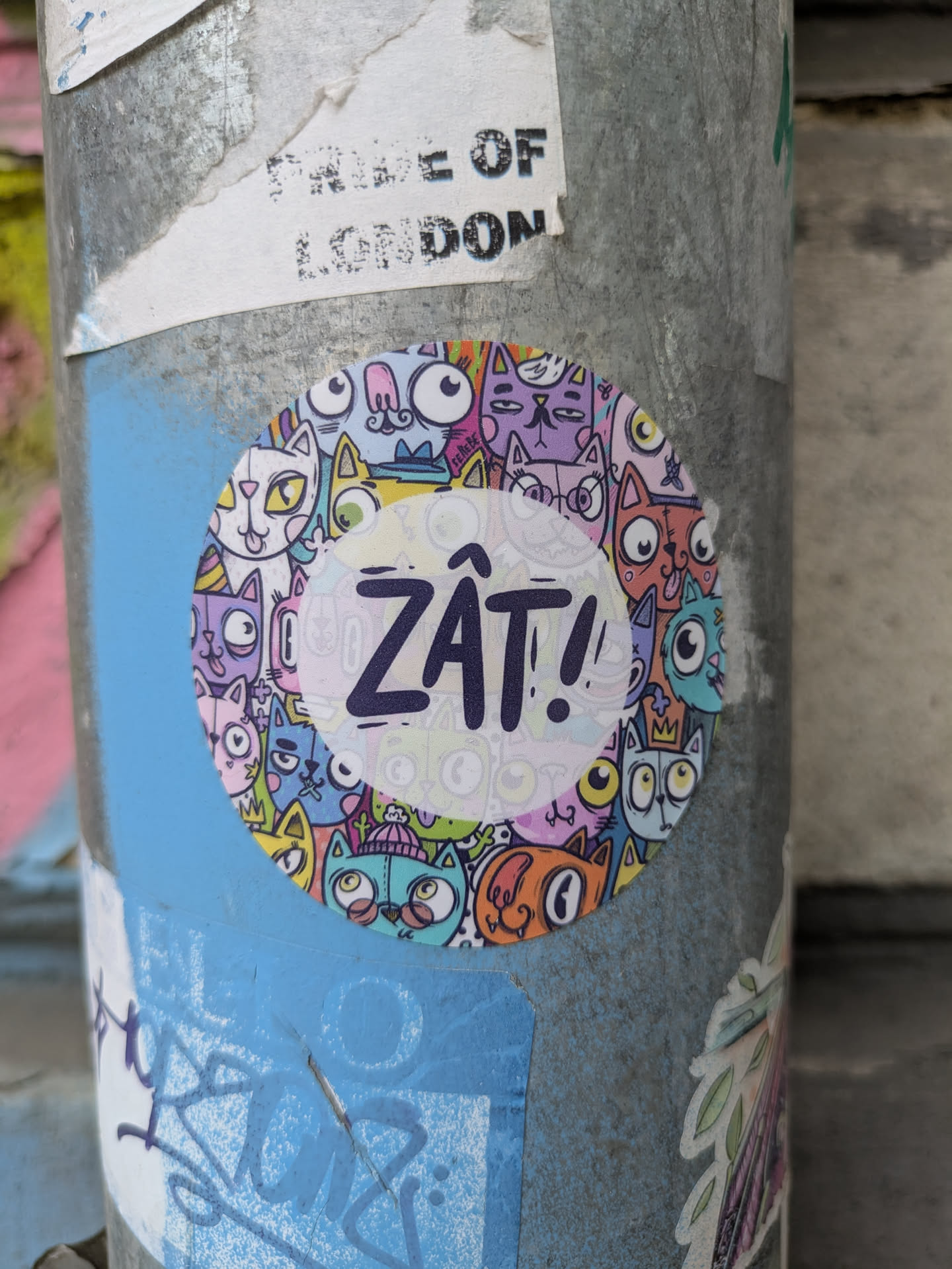 This is a round sticker affixed to a pole. The sticker is densely packed with cartoon cats of various colors and expressions. In the center, the word "ZÂT!" is written in bold, purple letters.