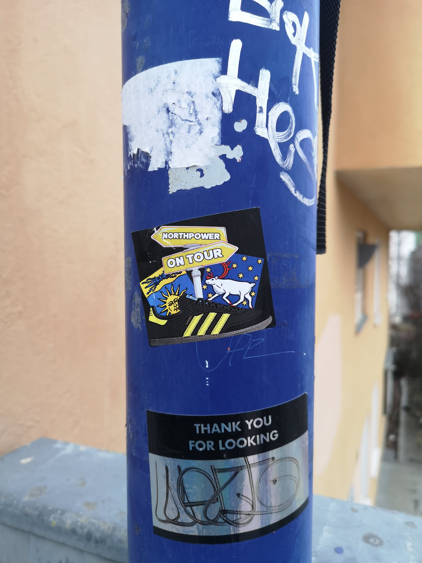 The sticker is rectangular with a black background, featuring a vibrant and detailed illustration. At the top, two yellow arrow-shaped signs point to the left, with 'NORTHPOWER' on the upper arrow and 'ON TOUR' on the lower one. Below these signs, a black Adidas Samba shoe with three prominent yellow stripes and a yellow sole is depicted, facing right. The background behind the shoe is split into two distinct halves: the left side showcases a stylized yellow sun with rays against a blue sky, while the right side features a white reindeer with red antlers and hooves, standing against a dark blue background dotted with numerous small yellow stars. The overall design suggests a journey or adventure with a northern or Nordic theme.