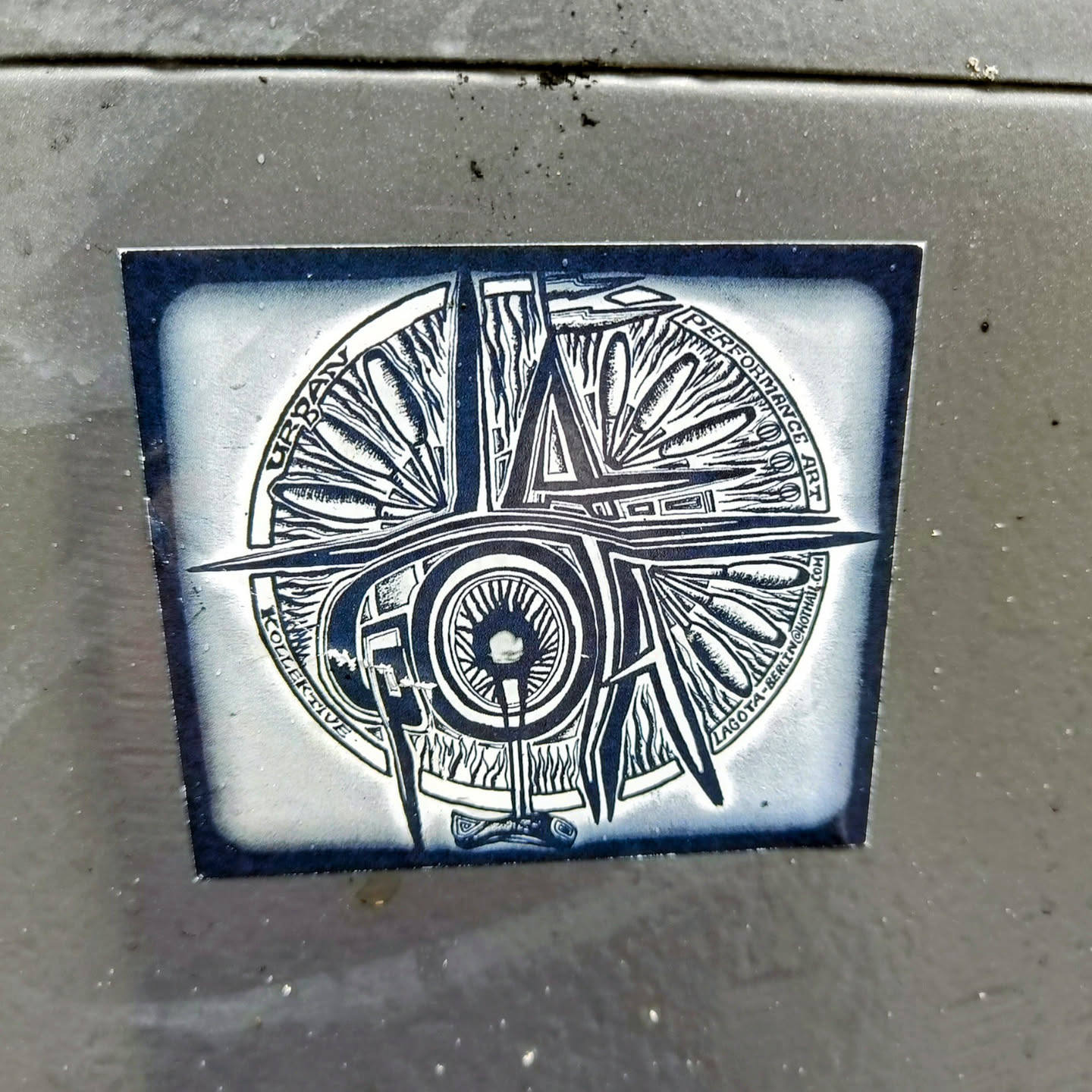 A sticker featuring a circular design with the word LAGOS in the center. The design incorporates elements suggestive of urban life and performance art.  The text around the circle reads "Urban Collective Performance Art Lagos Berlin".