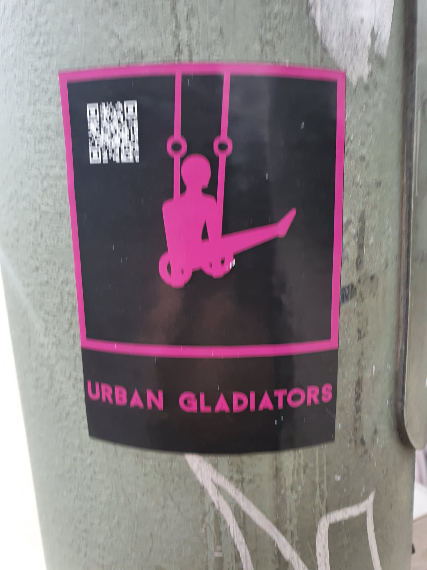 A black and pink sticker featuring a silhouette of a person performing on rings. The text 'Urban Gladiators' is visible at the bottom. A QR code is present at the top left corner.