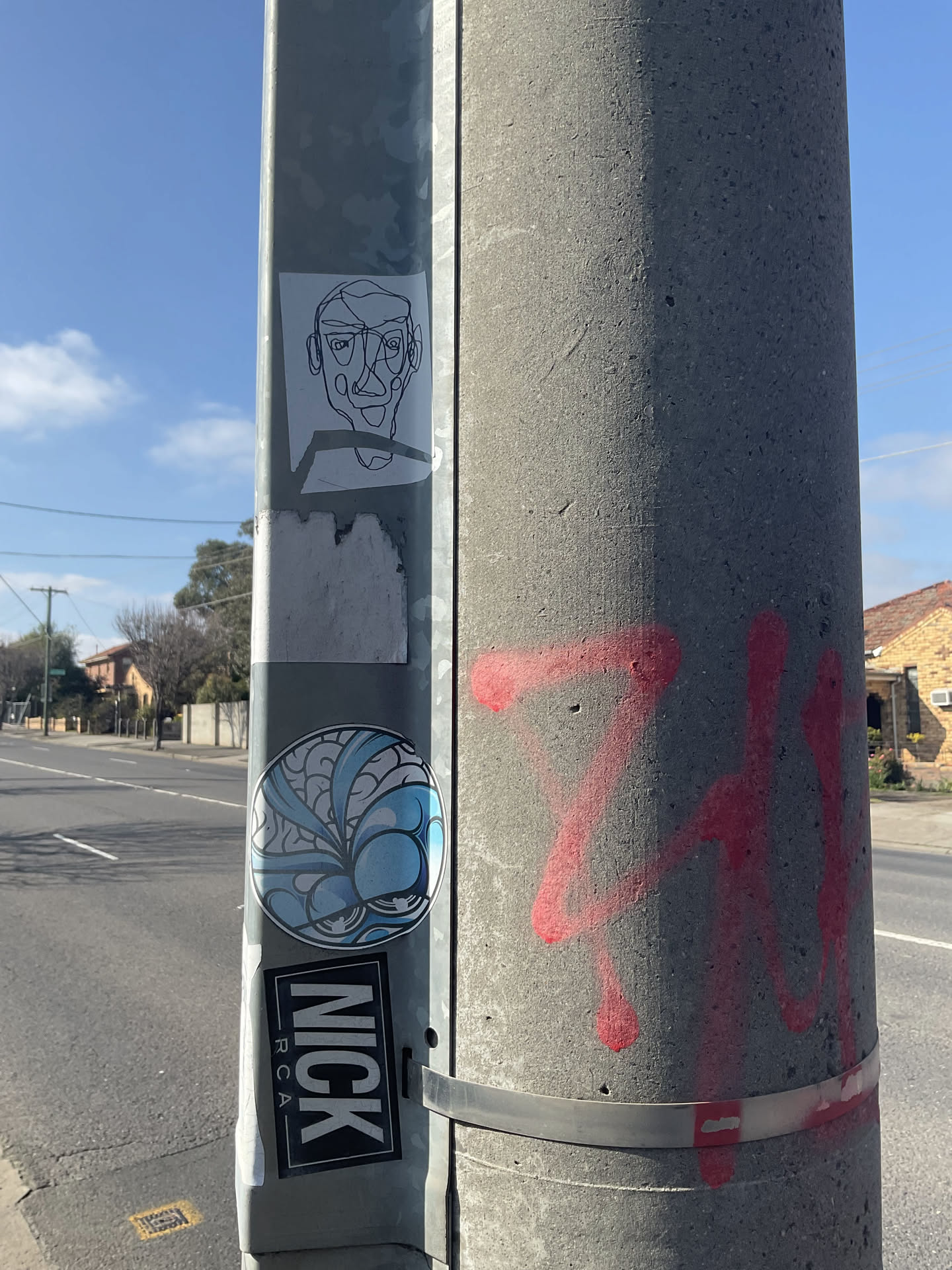 A round sticker placed on a metal post, featuring black-outlined artwork shaded in various tones of light blue, deep blue, and white. The design consists of swirling, shell-like segments in the upper portion and a pair of heavy-lidded or sleepy eyes integrated into rounded organic shapes at the bottom.