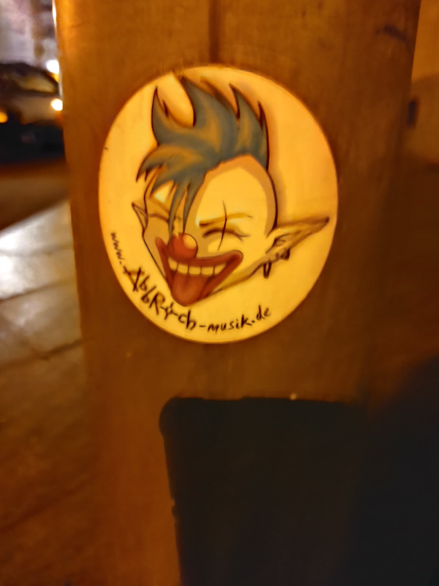 Round sticker featuring a cartoon illustration of a clown with blue spiky hair, a red nose, and a wide, toothy grin. The clown's tongue is sticking out.  The text 'alry-ch-musik.de' is visible on the sticker.