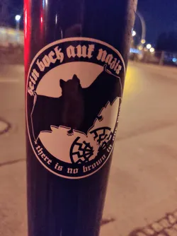 A round sticker with a bat and text in German and English. The German text translates to "No desire for Nazis". The English text says "There is no brown in the flag", referring to the Nazi colors.