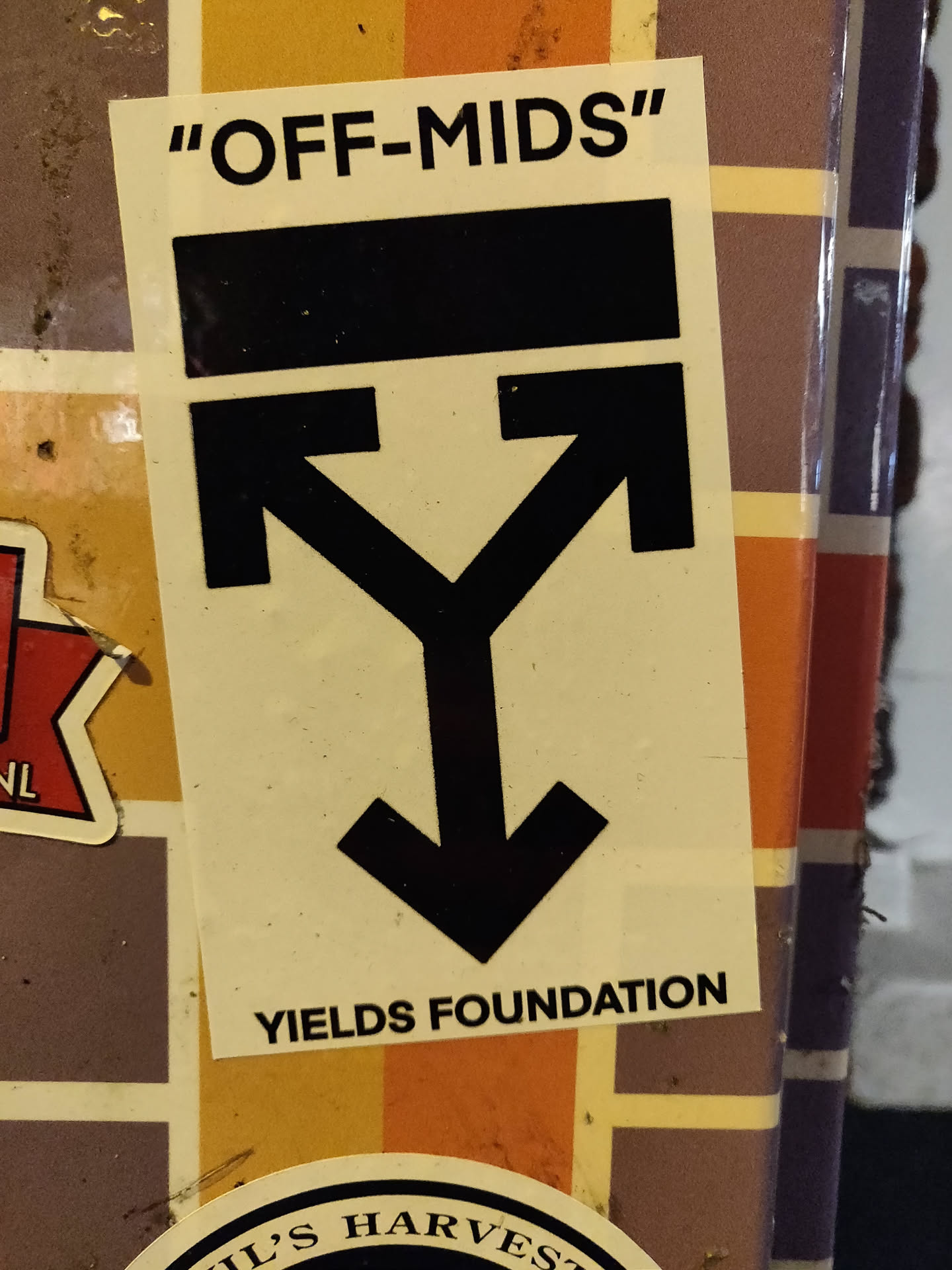 A beige sticker with black text and a symbol. The text says "OFF-MIDS" at the top and "YIELDS FOUNDATION" at the bottom. The symbol is a Y shape with arrows pointing up and down.