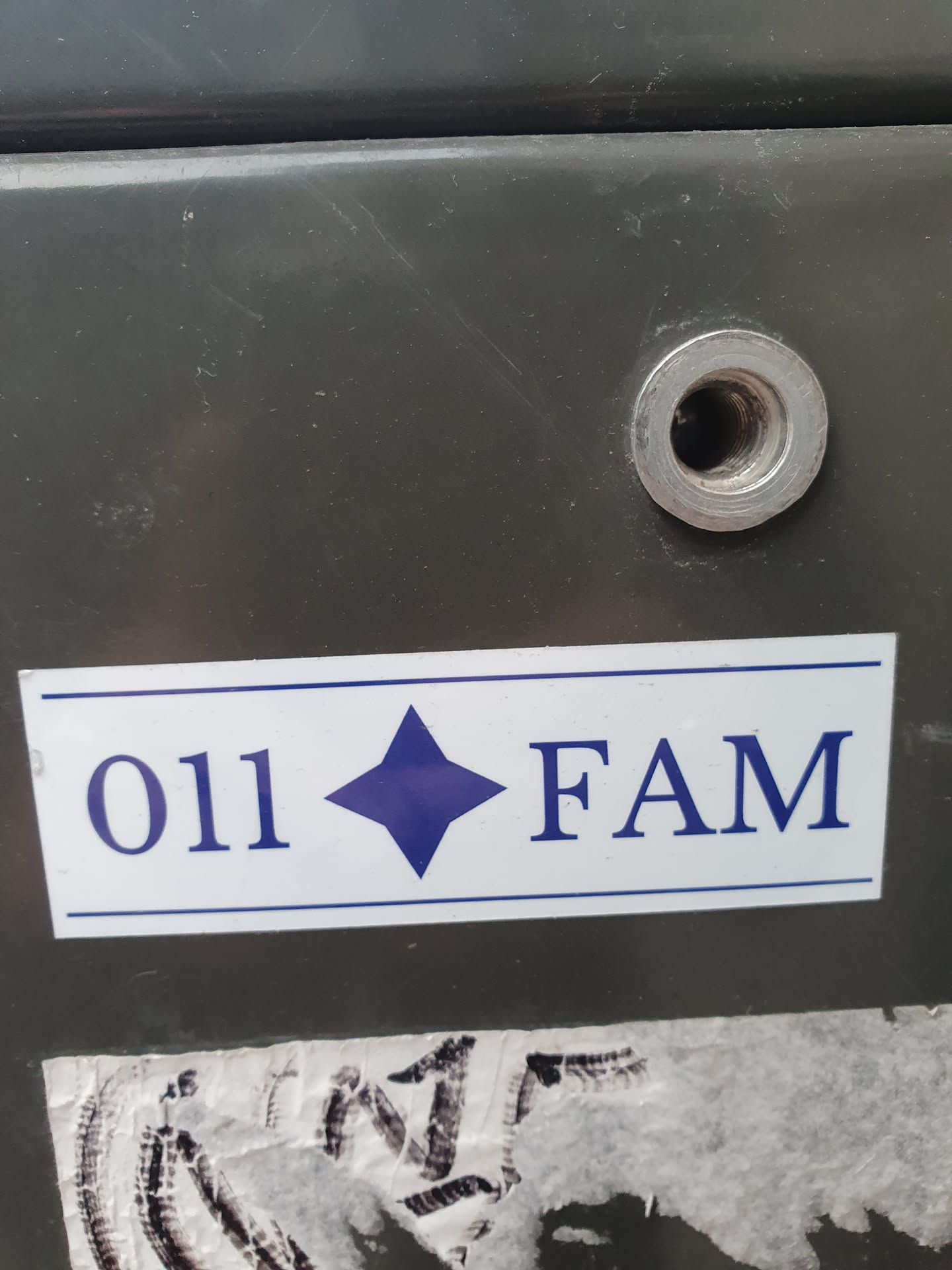 A sticker with the code 011, a blue diamond symbol, and the letters FAM. The sticker is rectangular and has a white background with dark blue text and symbol.