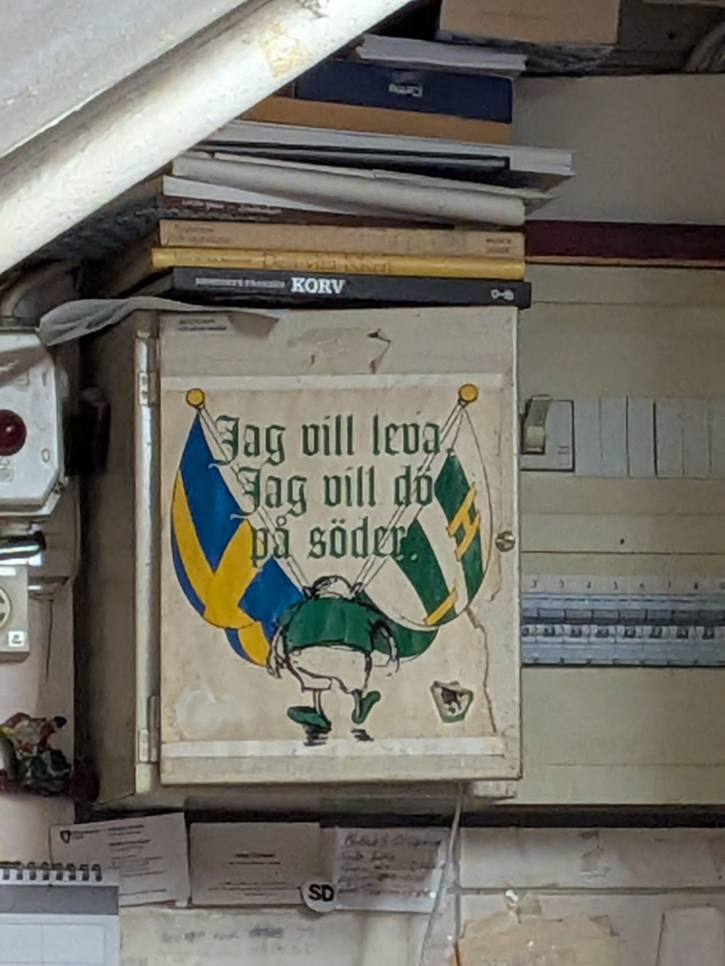 A large, rectangular sticker with a cream-colored background, showing signs of wear and peeling at the edges. It features a cartoon illustration of a supporter from behind, wearing a green shirt and white shorts, holding two crossed flags: the Swedish flag (blue and yellow) on the left, and a green and white striped flag with a yellow 'H' (Hammarby) on the right. Above the illustration, the text 'Jag vill leva Jag vill dö på söder.' is written in a green gothic-style font.