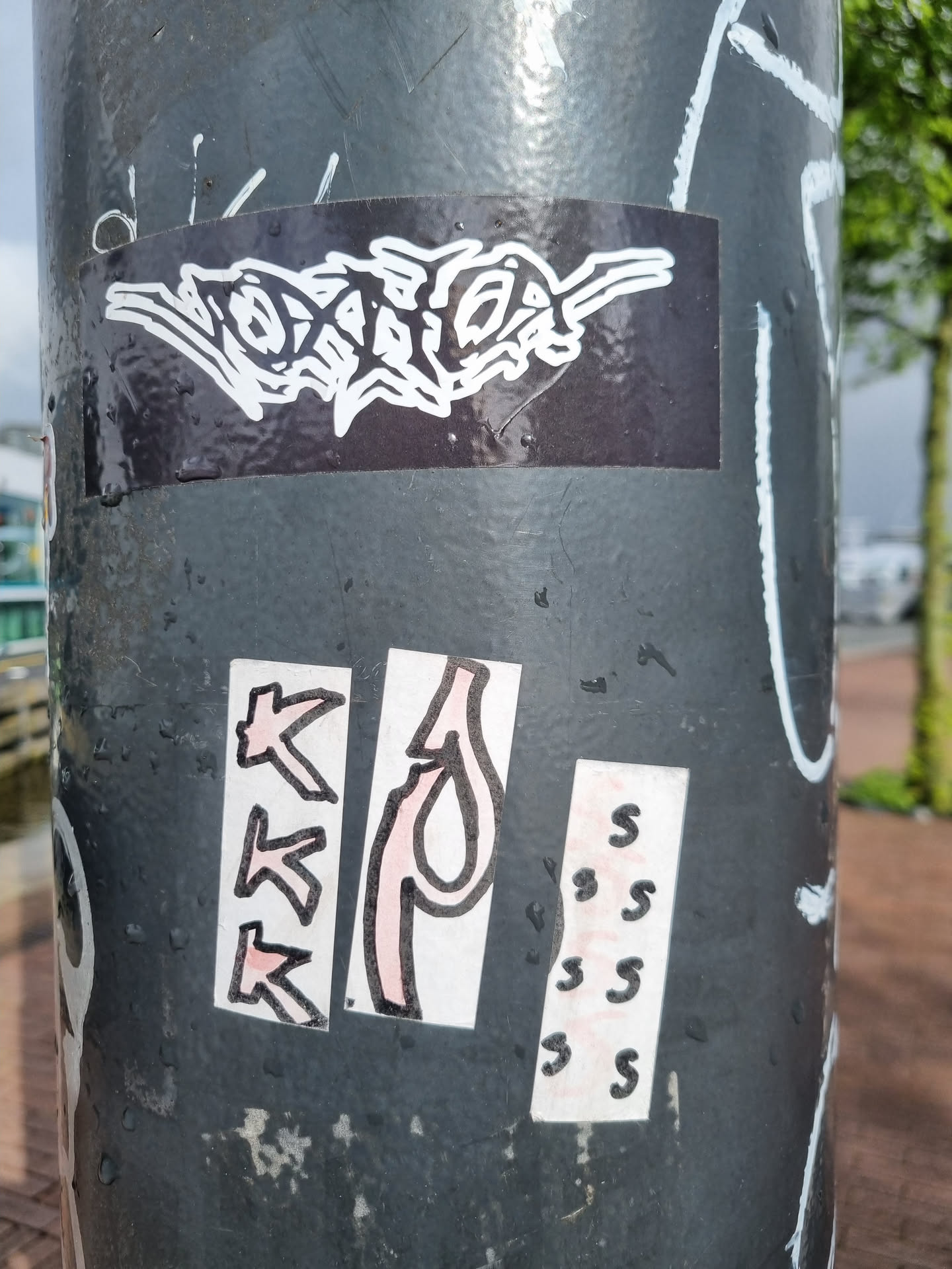 The sticker features a minimalist, abstract design of an insect-like creature, predominantly in black and white, with the insect's body consisting of a series of connected segments.  The overall style is graphic and slightly surreal.  There are other stickers on the same pole. 
