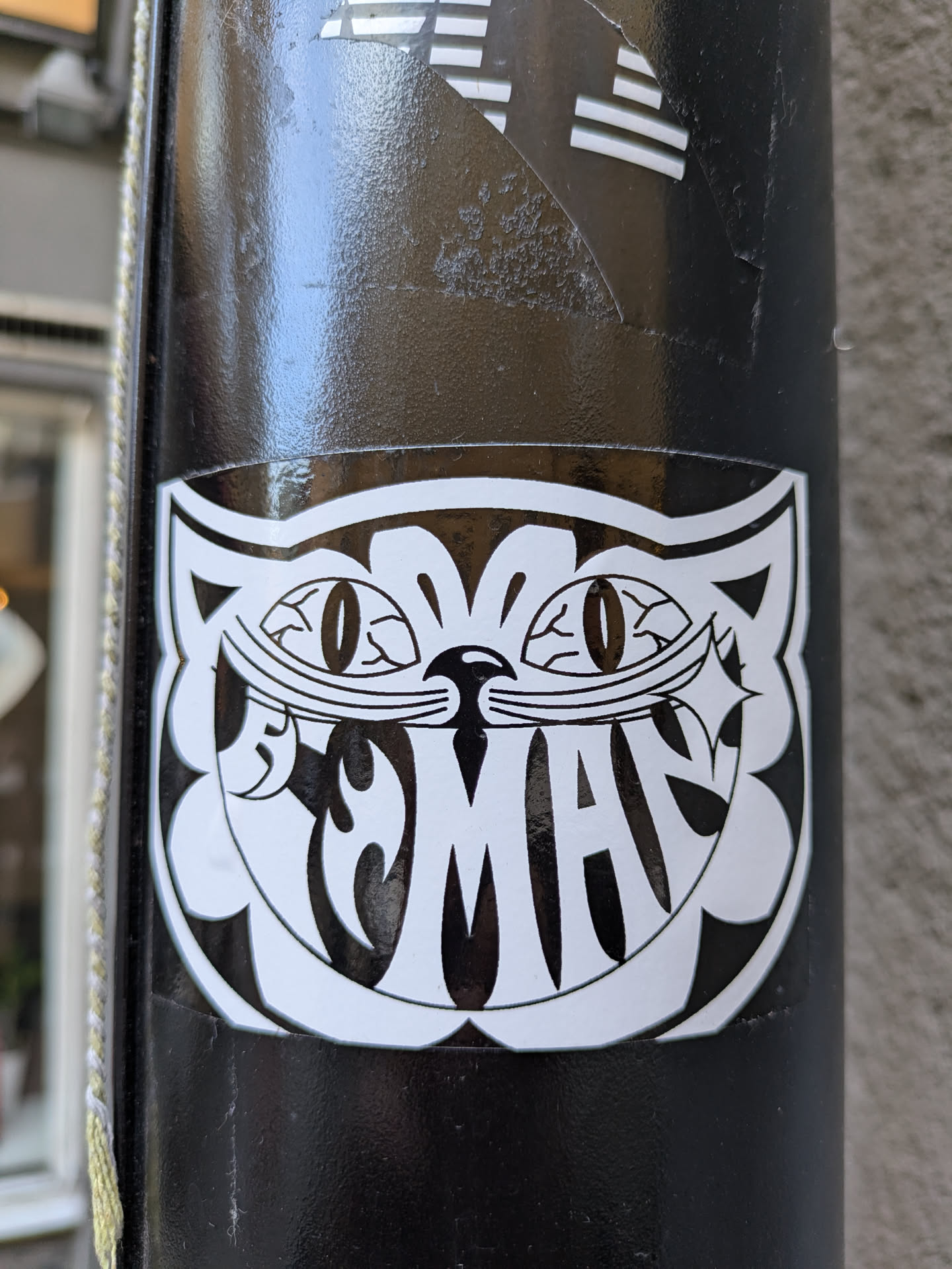 A black and white sticker featuring a stylized cat face with the word "Mad" written inside. The cat has large, oval eyes and a mischievous grin. The style is reminiscent of vintage cartoons or illustrations.