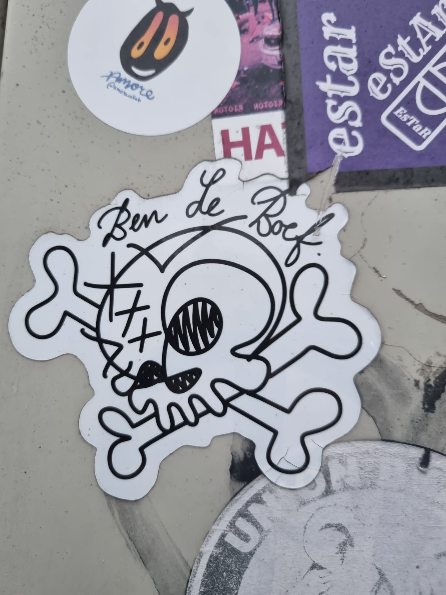 A black and white sticker featuring a cartoon skull and crossbones. The skull has X for eyes and a goofy expression. The artist's signature, "Ben Le Boeuf," is written in cursive above the skull. 