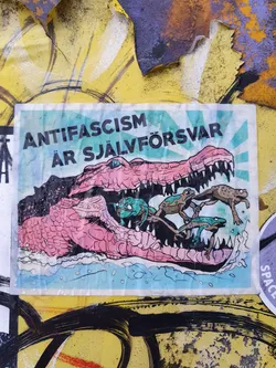 A sticker with an illustration of a crocodile with frogs in its mouth. The text on the sticker says "Anti-fascism är självförsvar" which translates to "Anti-fascism is self-defense" in Swedish.