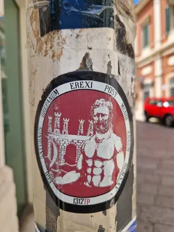 This round sticker features a red background with a white illustration of a muscular man with a beard who appears to be inspired by Roman iconography. He is situated in front of a structure that resembles a fortress or city gate. The surrounding text suggests a reference to a historical event or era. The number "1312TP" is printed at the bottom.
