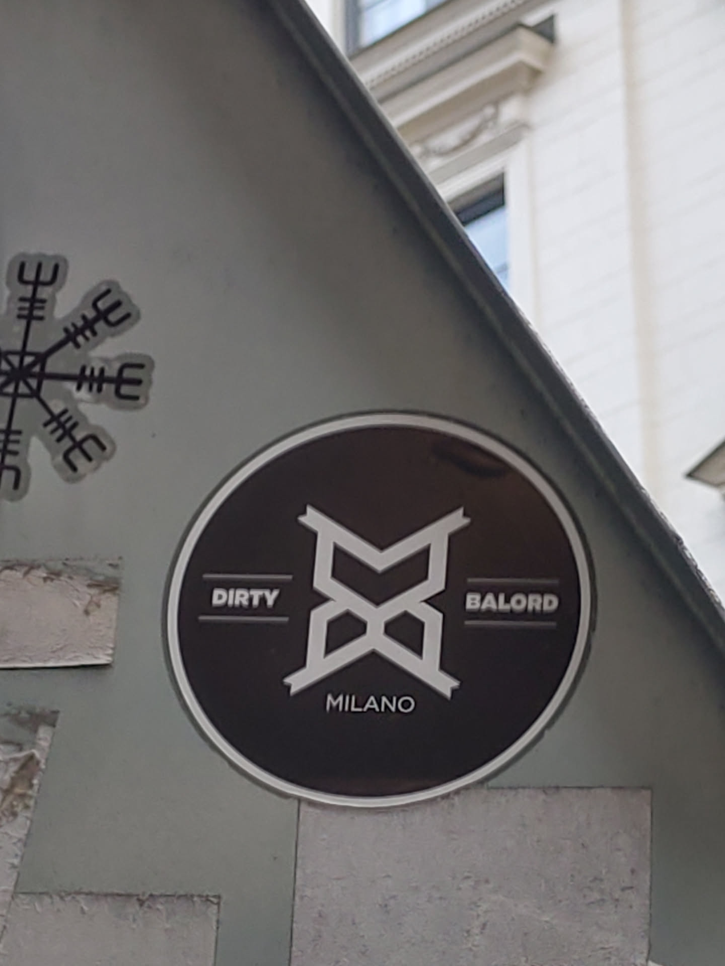 Round black and white sticker with a logo and text. The logo is a stylized "M" or "B" shape.  The text says "DIRTY" on the left, "BALORD" on the right, and "MILANO" at the bottom.