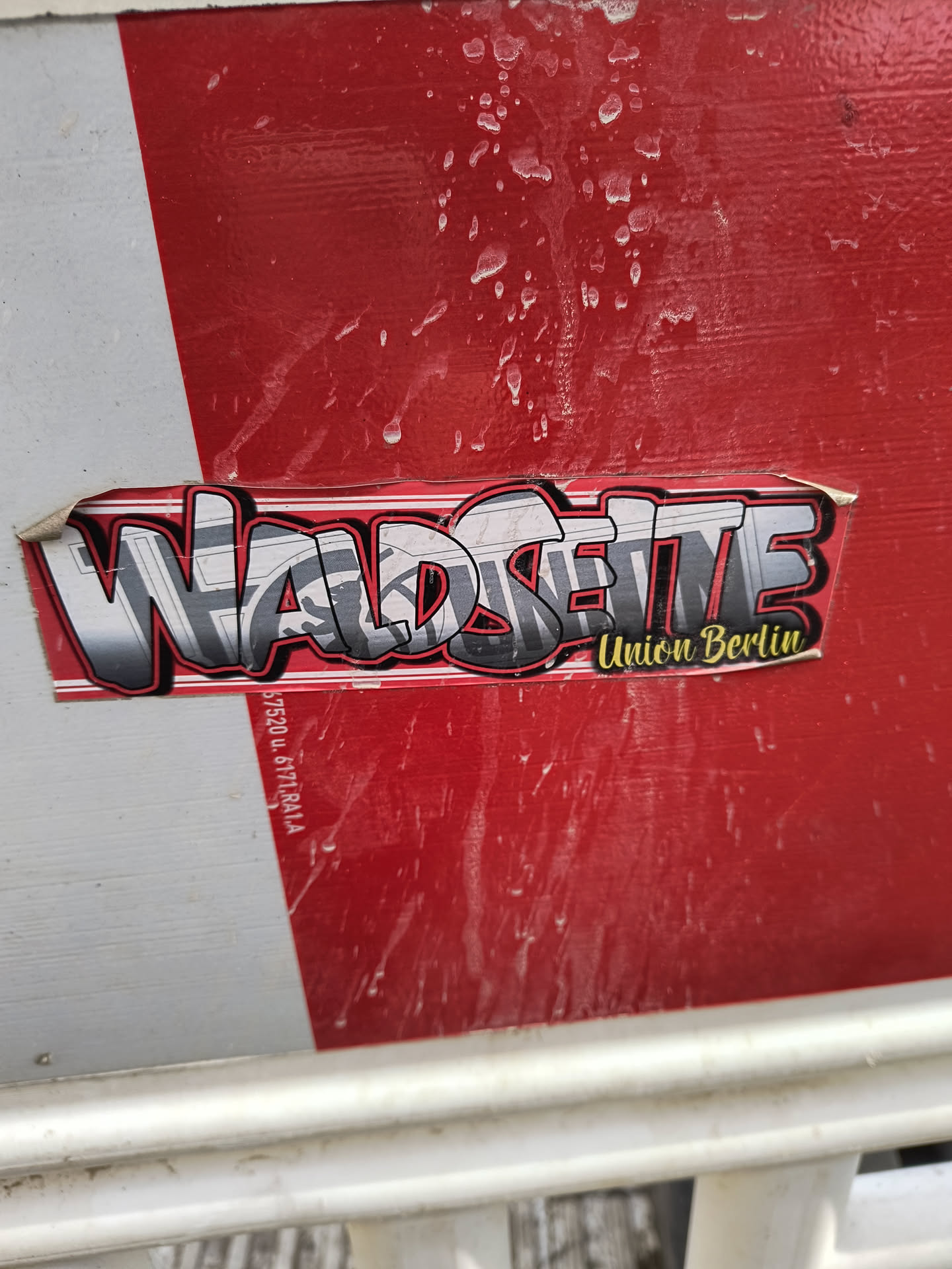 A sticker featuring the words "Waldseite Union Berlin" in a stylized graffiti font. The sticker is applied to a red surface, possibly a barrier or fence.