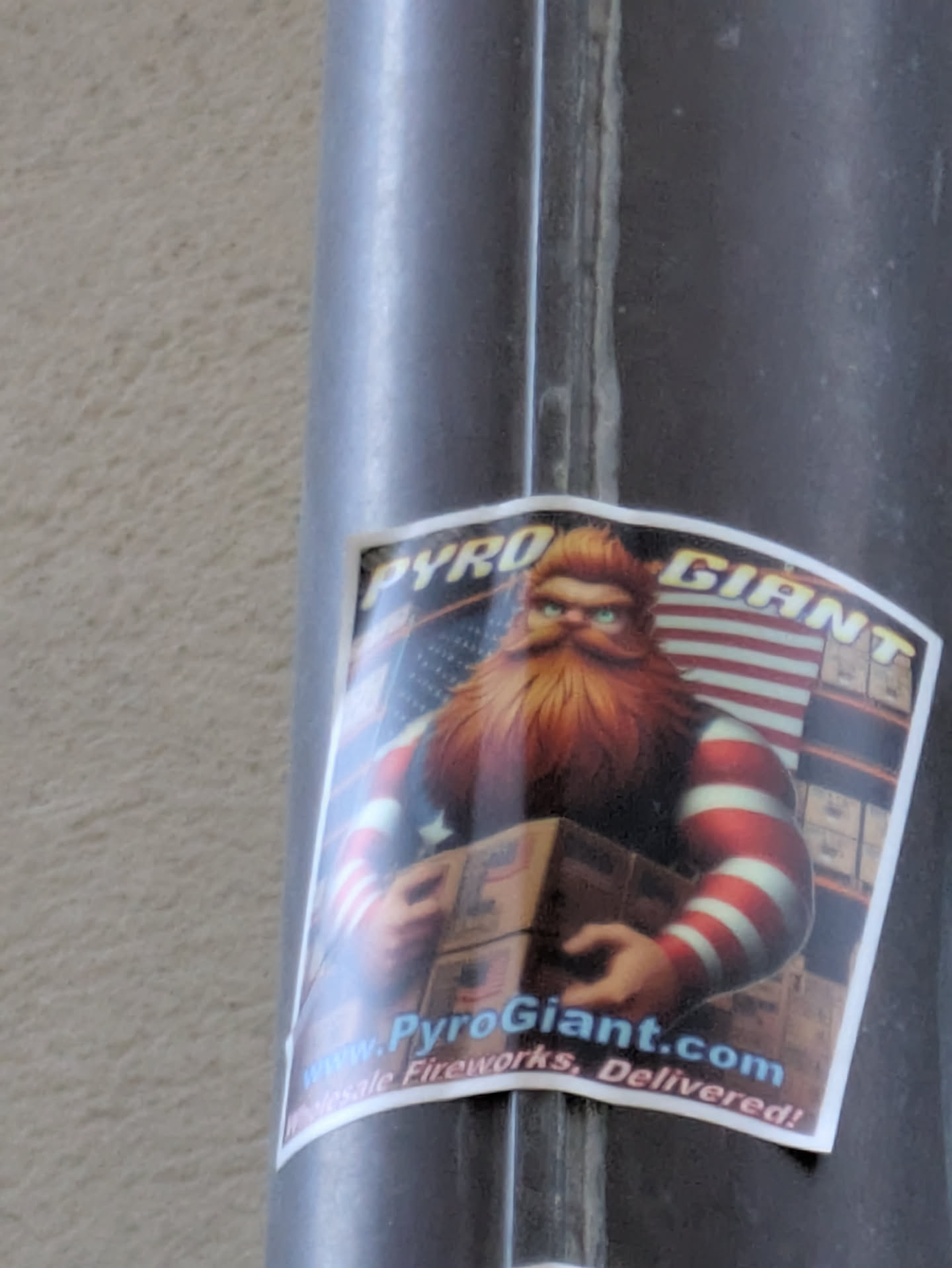 Sticker featuring a cartoon illustration of a bearded man in red and white striped sleeves holding boxes of fireworks.  The background includes an American flag and what appears to be a fireworks warehouse. The website www.PyroGiant.com is prominently displayed.