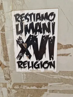 A black and white sticker with dripping text. The text says "Restiamo Umani XVI Religion". The sticker is attached to a wall.