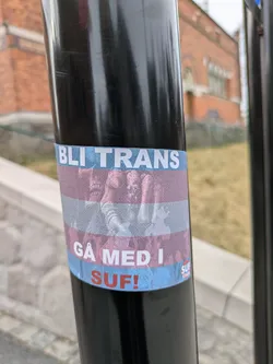 The sticker features the colors of the trans flag (light blue, pink, and white stripes) with text that reads "BLI TRANS GÅ MED I SUF!" and a crowd below the text.