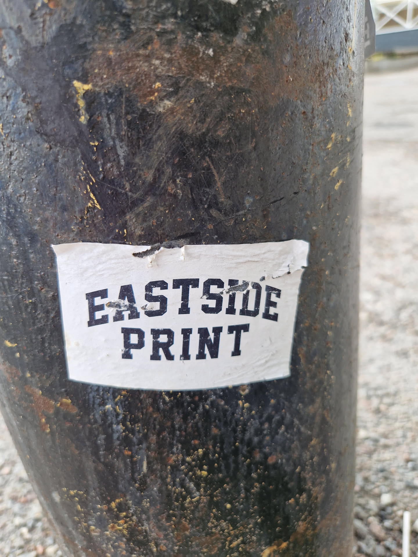 A simple sticker with the text "Eastside Print" in a dark-colored, sans-serif font on a white background affixed to a dark-colored pole.
