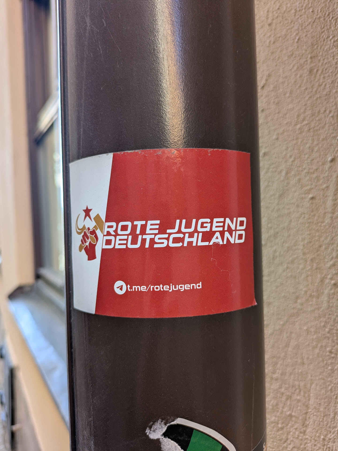 A red and white sticker on a pole with the text 'Rote Jugend Deutschland' and a logo featuring a fist holding a hammer and sickle. There is also a link to their Telegram channel.