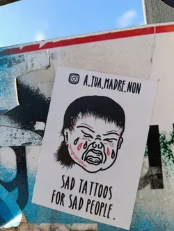 Sticker featuring a drawing of a crying baby with stitches on its face. The text on the sticker says "Sad tattoos for sad people." An Instagram handle is also present.