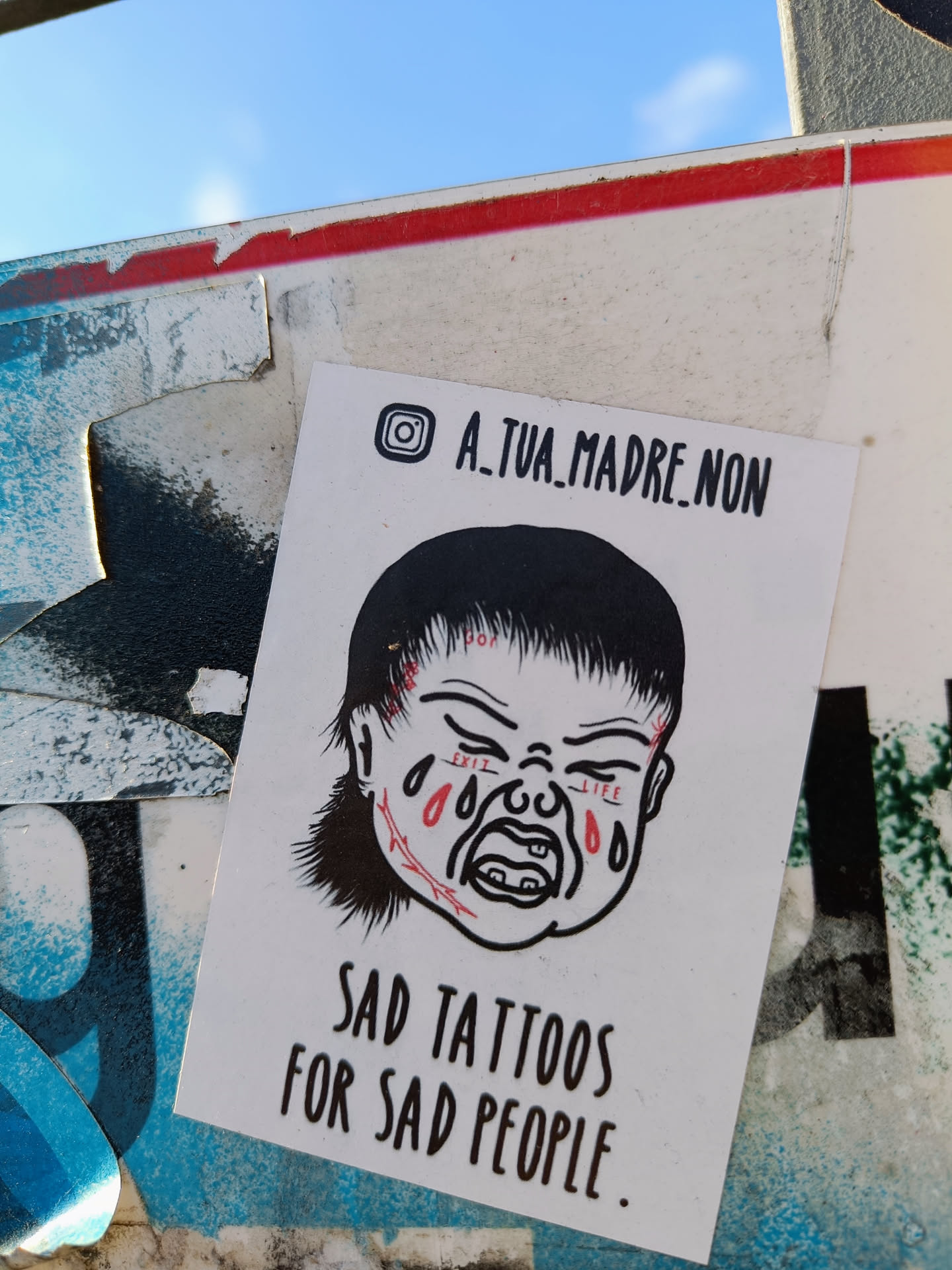 Sticker featuring a drawing of a crying baby with stitches on its face. The text on the sticker says "Sad tattoos for sad people." An Instagram handle is also present.