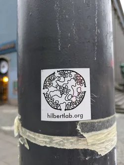 A circular sticker featuring an abstract black and white line drawing. The text 'hilbertlab.org' is printed at the bottom of the sticker.