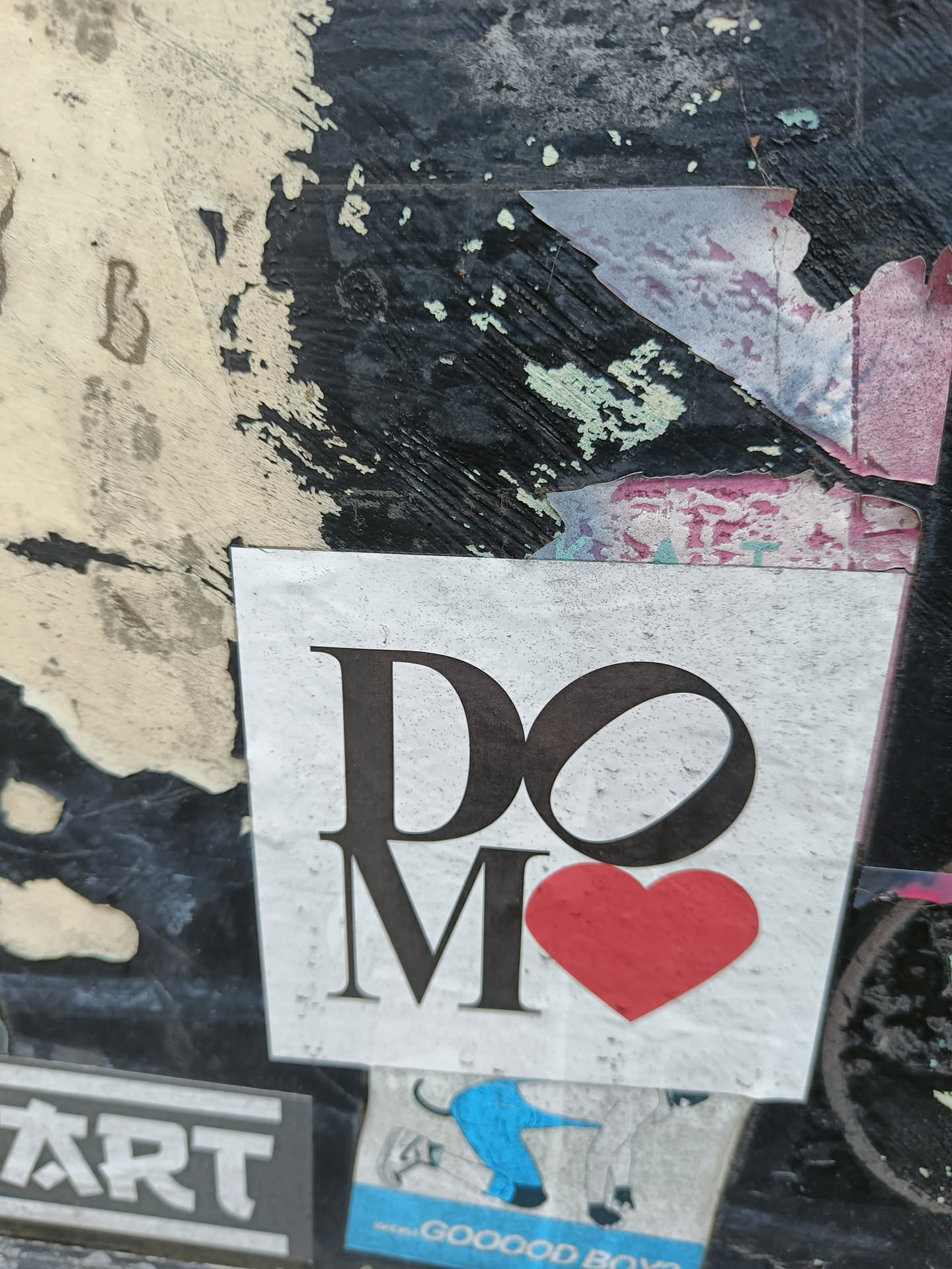 A minimalist sticker with the text 'DO MORE' and a red heart. The sticker is affixed to a grunge background with other stickers and markings.