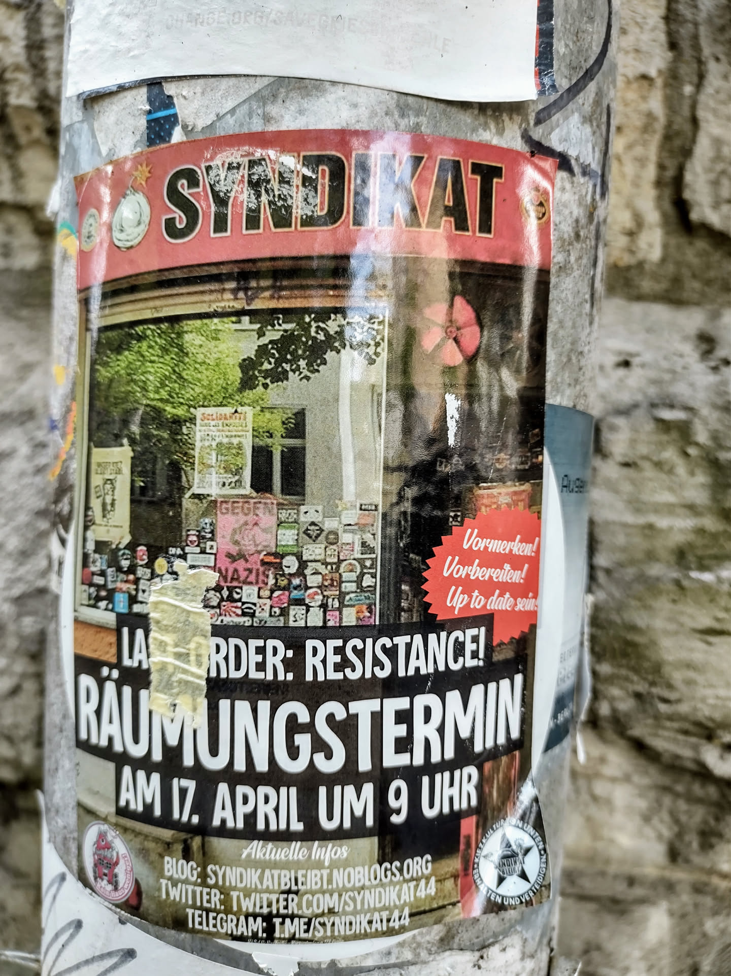 A sticker on a pole showing an eviction notice from Syndikat 44. The sticker shows images of the building and the text 'LA ORDER: RESISTANCE!' with the date and time of the eviction. It includes social media links.