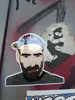 A sticker featuring an illustration of a man with a beard, wearing a hat with the Supreme logo on it. The style is somewhat cartoonish and features a detailed depiction of his facial hair. 