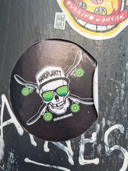 A round black sticker with a skull wearing a hat that says "Handplantt" and sunglasses. The skull is holding four skateboards. The text "Skateboarding" is written at the bottom. 