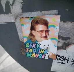 A sticker featuring a man with a mullet and a small white dog. The background is pastel pink with rainbows and clouds. The text on the sticker says "SEXY TAB IHR MÄUSE" in colorful letters.