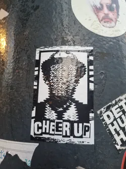 Black and white sticker with a distorted image of a person and the words "CHEER UP" at the bottom. The style is reminiscent of glitch art or digital distortion.