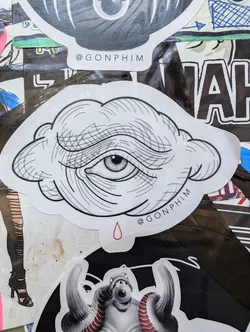 A monochrome illustration of an eye inside a cloud with a single red teardrop below. The style is reminiscent of traditional tattoo flash. The artist's Instagram handle is visible on the sticker.